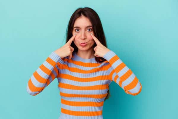 Mulher apontando para os olhos após ter feito cirurgia refrativa.