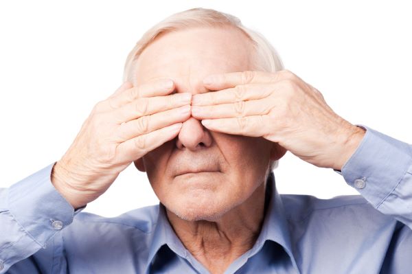 Homem sênior cobrindo os olhos com as mãos, aparentando dor ocular.