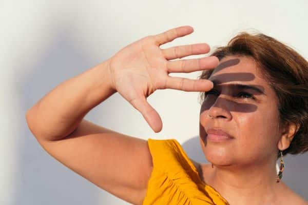 Um dos fatores de risco para o desenvolvimento é não usar proteção ocular durante exposição aos raios UV, como faz uma senhora tapando o rosto com a mão.