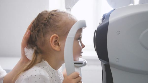 Menina realizando exame oftalmológico em aparelho.